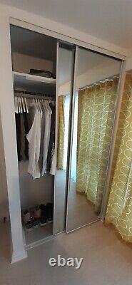 Mirrored wardrobe sliding doors with tracks, shelves, and black hanging rail
